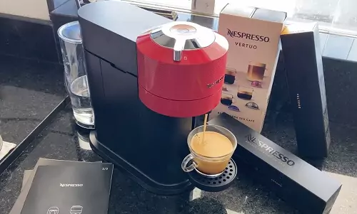 Nespresso Next em cima de pia de mármore preta, com uma xícara pequena na bandeja e pacotes de cápsulas Nespresso atrás.
