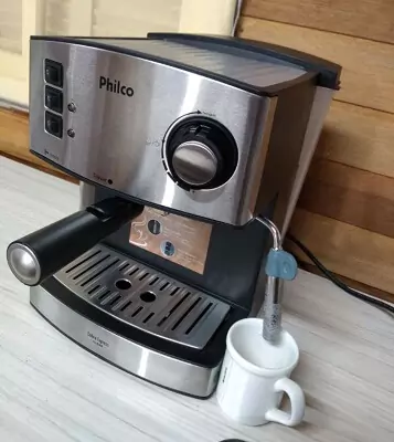 Philco Coffee 15 em mesa de madeira, com filtro acoplado e caneca branca embaixo do espumador de leite.