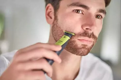 Homem utilizando OneBlade para desenhar a linha da bochecha da barba em frente ao espelho.