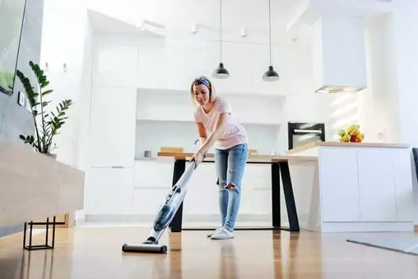 Mulher utilizando aspirador de pó vertical sem fio para aspirar a cozinha.