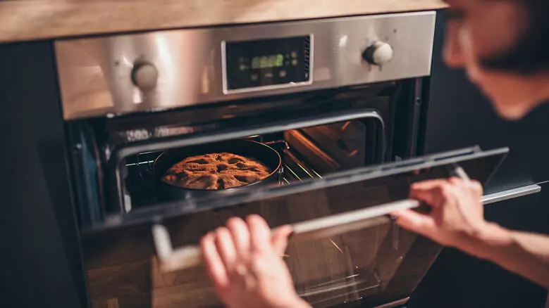 Imagem de abertura do post sobre o melhor forno elétrico de embutir: Mulher abrindo forno elétrico com bolo dentro
