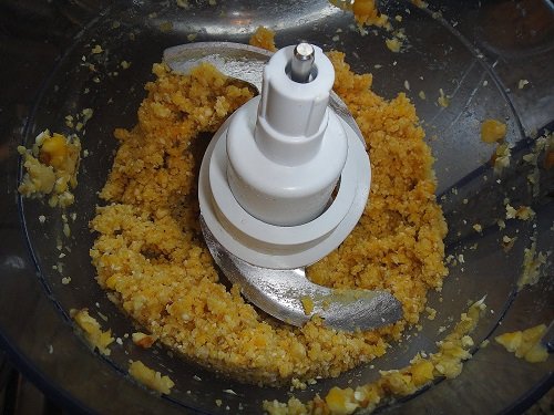 Foco em faca de multiprocessador processando ingrediente amarelo em tigela.