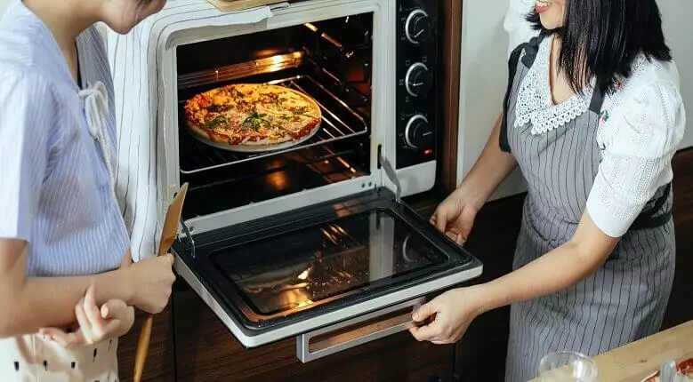 Abertura do post sobre o melhor forno elétrico: Mulher e homem abrindo porta de forno elétrico com uma pizza dentro.