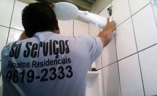 Homem instalando chuveiro elétrico em banheiro com azulejo branco.