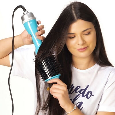 Mulher morena usando uma escova secadora azul para secar os cabelos.