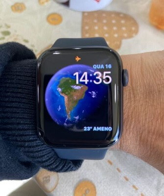Foco no Apple Watch Series 6 preso no pulso, com um globo terrestre como fundo de tela.