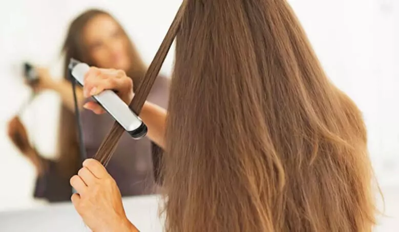 Abertura do post sobre a melhor chapinha de cabelo: Mulher com cabelo longo utilizando prancha de cabelo em frente ao espelho