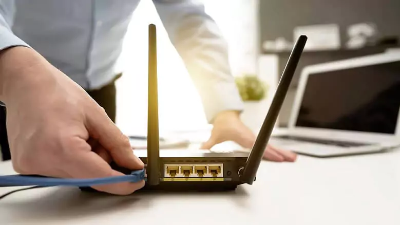 Abertura do post sobre o melhor roteador wi-fi: Mão masculina conectando o cabo de internet em um roteador.