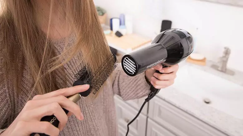 Abertura do post sobre o melhor secador de cabelo: Mulher de cabelo castanho secando o cabelo com pente e escova.