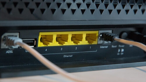 Foco na parte traseira de um roteador, detalhando as portas LAN amarelas, com cabos ligados na entrada internet.