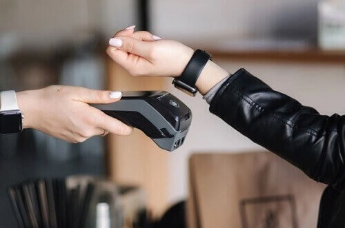 Mulher utilizando relógio inteligente para fazer um pagamento em maquininha de recebimento.