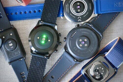 Quatro smartwatchs apoiados de cabeça para baixo, destacando seus sensores de batimentos cardíacos.