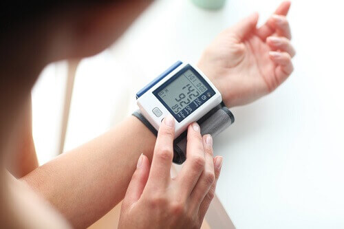 Mulher medindo a pressão utilizando medidor de pressão de pulso.
