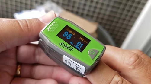 Foco no G-Tech Pediátrico ligado a um dedo indicador, marcando 95 de saturação e 61 bpm.