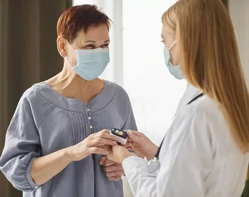 Enfermeira medindo a saturação de paciente idosa usando máscara.