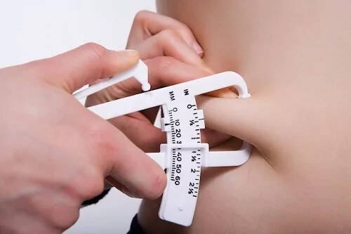 Foco em adipômetro medindo a gordura da região da barriga.
