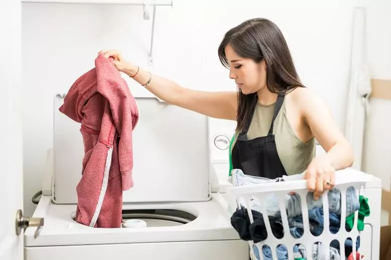 Abertura do post sobre o melhor tanquinho de lavar roupas: Mulher tirando blusa de tanquinho enquanto segura um cesto.