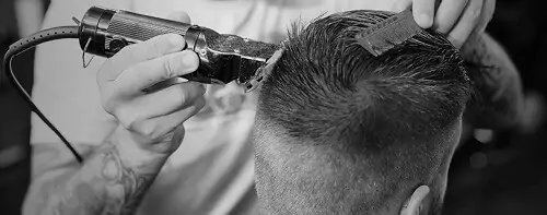 Foto em preto e branco de barbeiro fazendo o movimento em C para cortar cabelo de cliente.