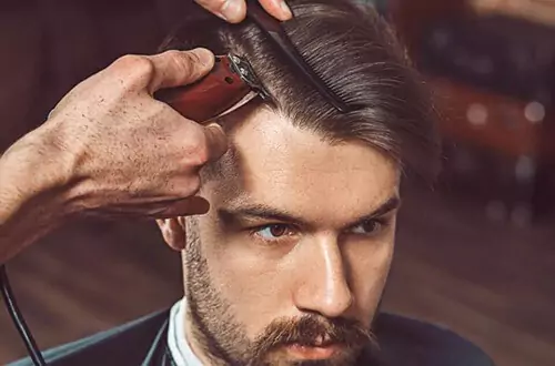 Barbeiro fazendo detalhe em cabelo de homem com uma máquina de acabamento.