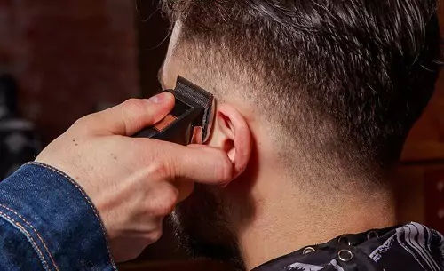 Barbeiro utilizando o movimento reto de parede para cortar a lateral do cabelo de um homem em efeito degradê.