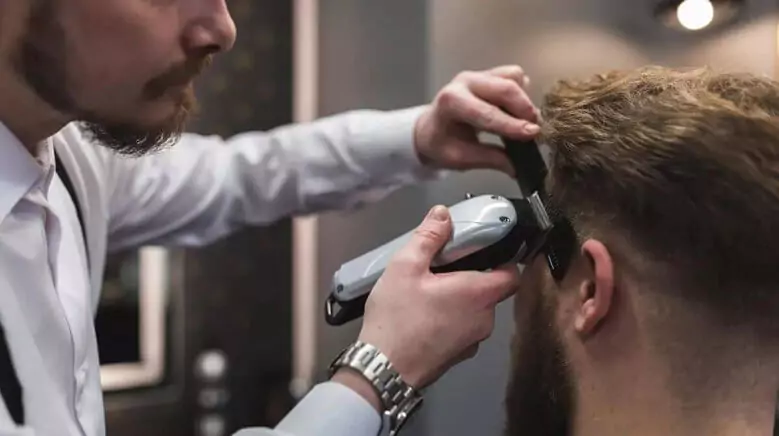 Abertura do post sobre a melhor máquina de cortar cabelo profissional: Visão lateral de barbeiro fazer corte degradê em homem