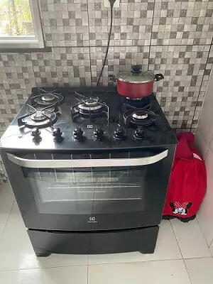 Electrolux 76GS em cozinha com azulejo cinza e piso branco, com panela vermelha no queimador posterior.