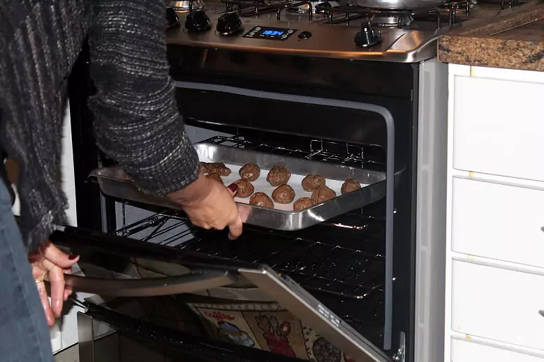 Abertura do post sobre o melhor fogão 5 bocas: Homem retirando travessa com biscoitos de dentro de forno de fogão.